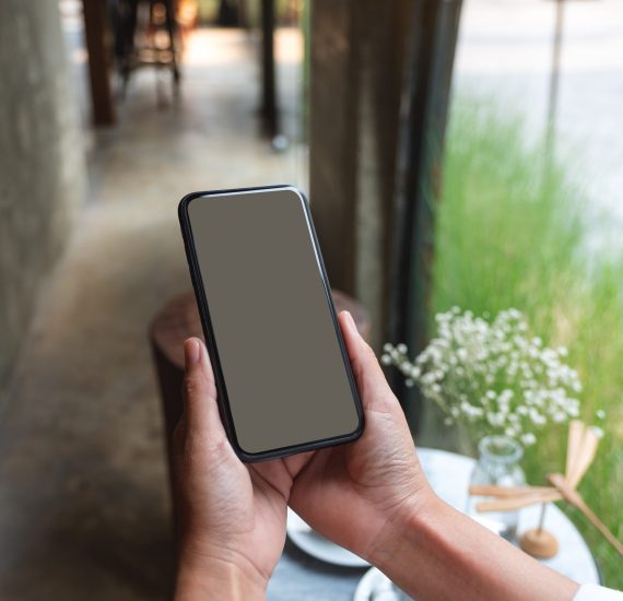 Mockup image of a woman holding mobile phone with blank desktop screen in cafe